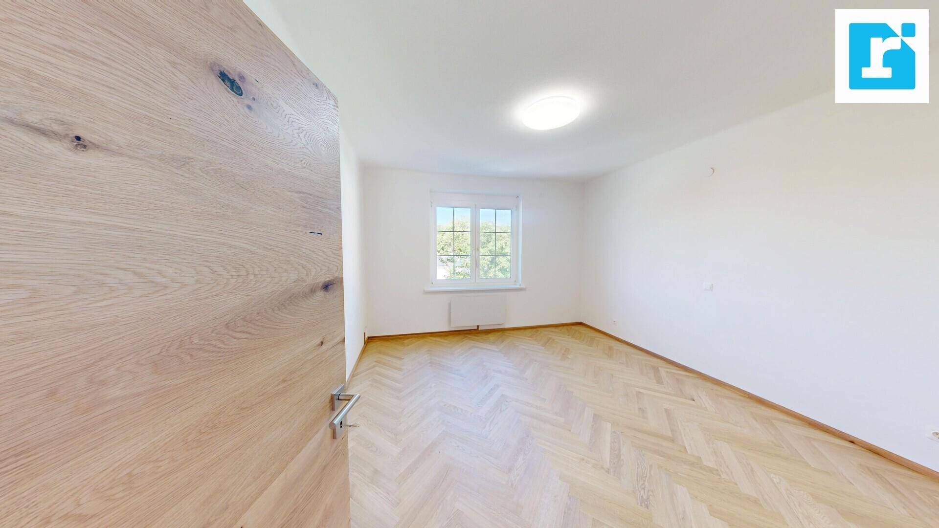 Geräumiges Schlafzimmer mit hellem Fischgrätparkett und großem Fenster.