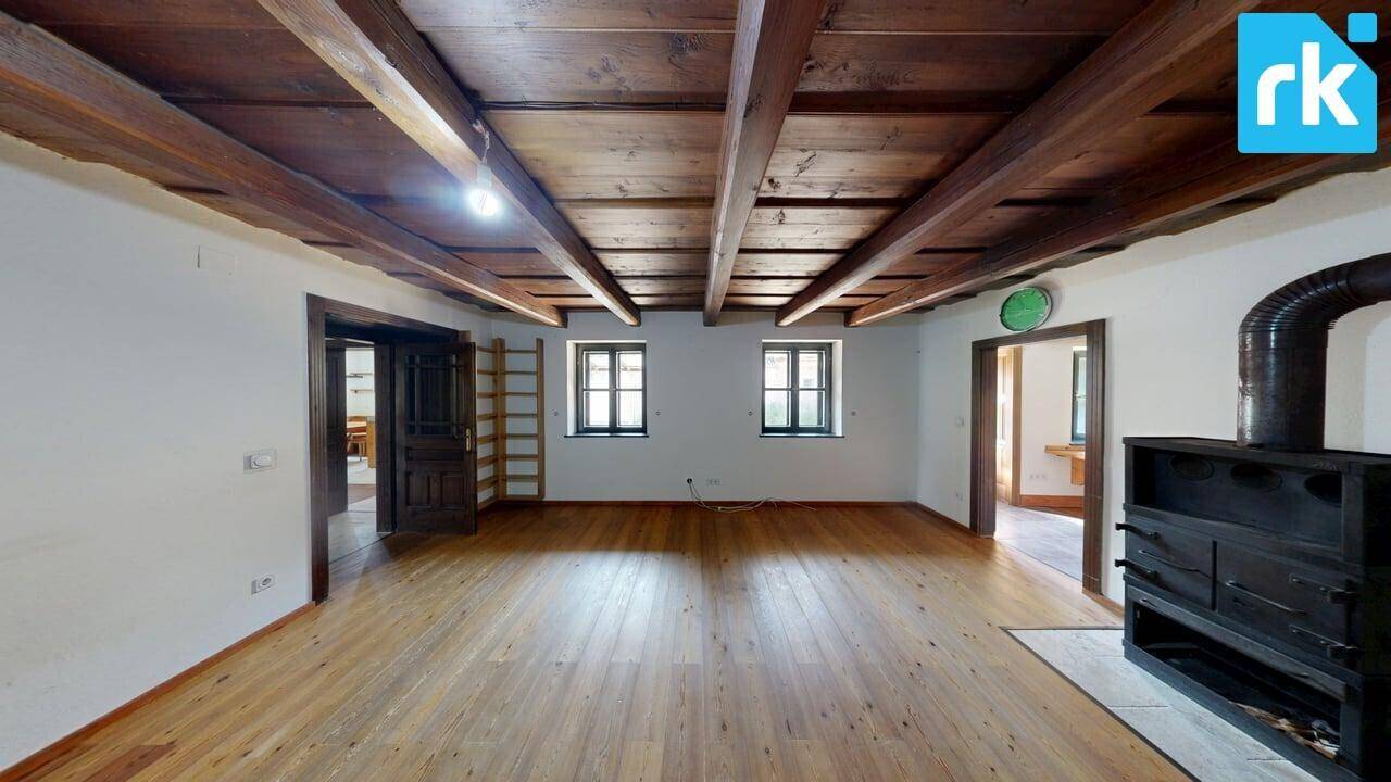 Geräumiges Wohnzimmer mit sichtbaren Holzbalken, Holzboden und mehreren Fenstern.