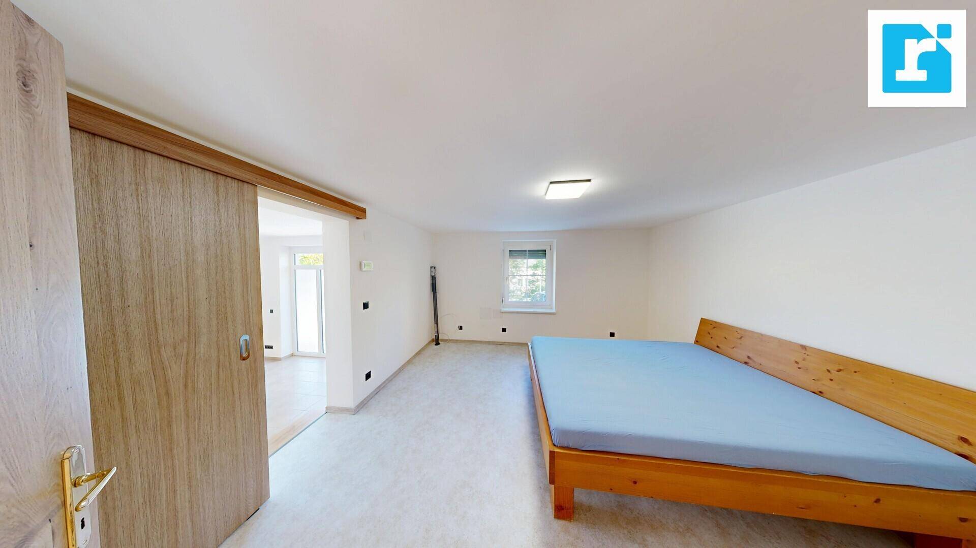 Helles Schlafzimmer mit Holzbett und Schiebetür, die zu einem weiteren Wohnbereich führt.