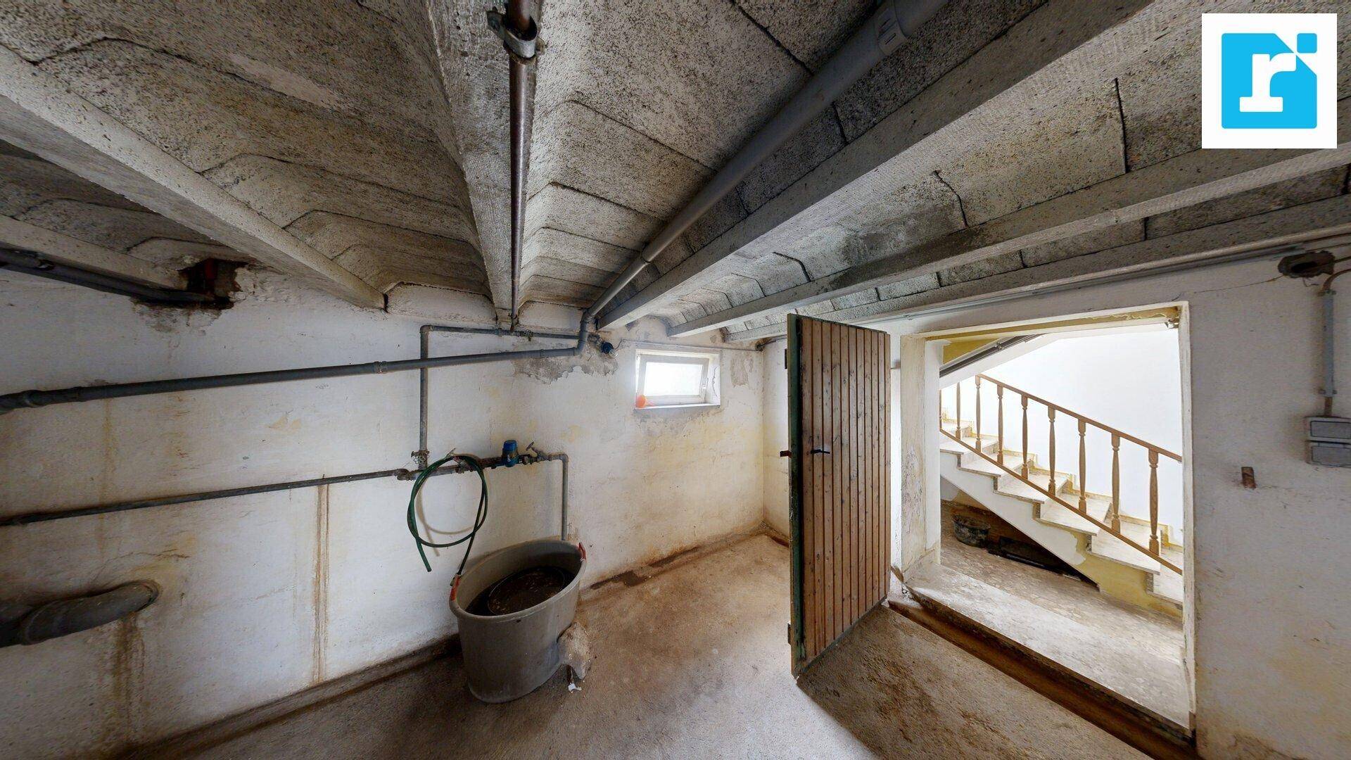 Geräumiger Kellerraum mit Betonboden, sichtbaren Rohren und einem kleinen Fenster, das Tageslicht hereinlässt.