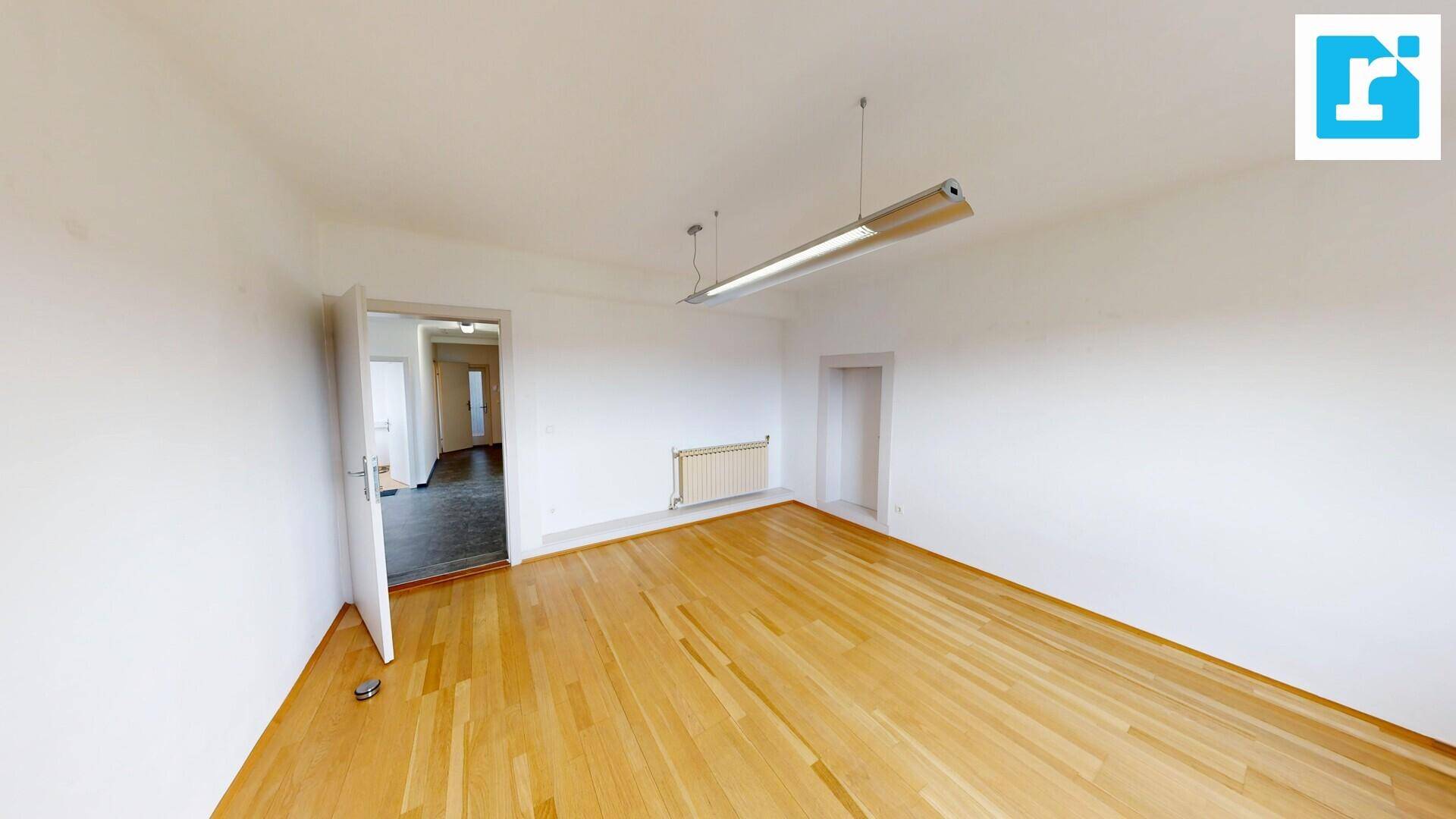 Leeres Büro mit Holzboden, weißen Wänden und einer offenen Tür zu einem weiteren Raum, bietet viel Potenzial.