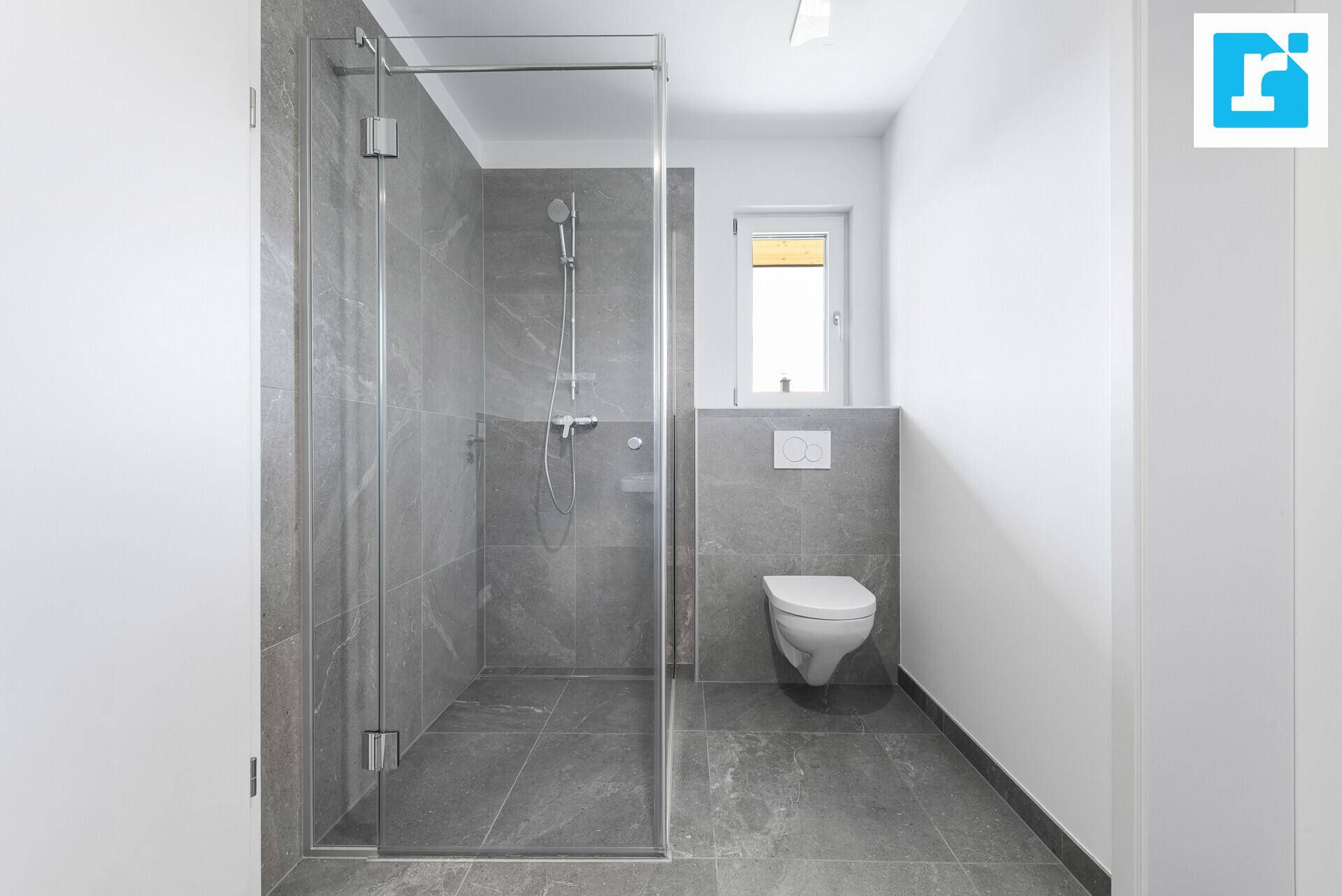Modernes Badezimmer mit großer Dusche, Wand-WC und grauen Fliesen.