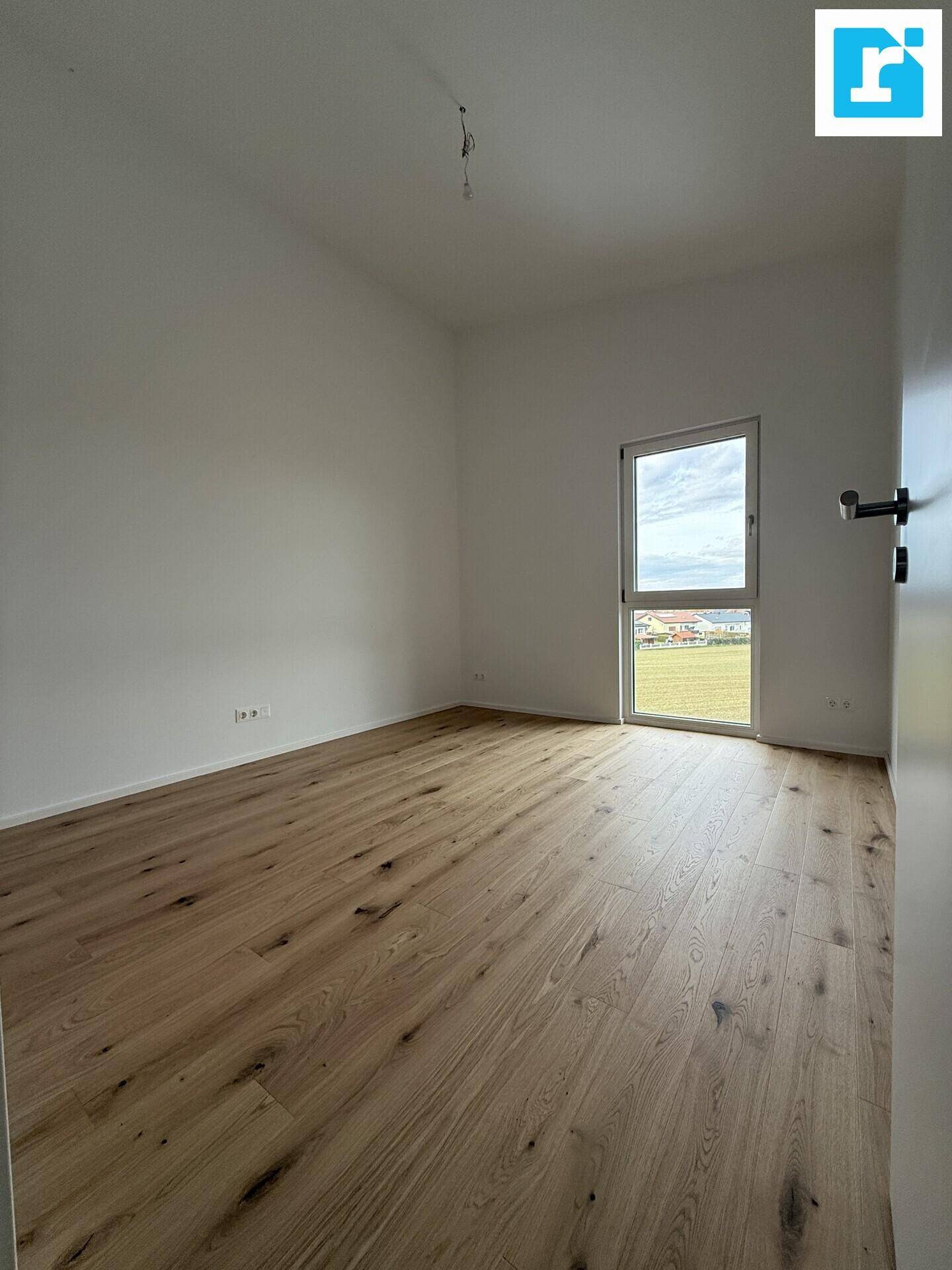 Geräumiges Schlafzimmer mit Parkettboden und Fenster mit Blick ins Grüne.