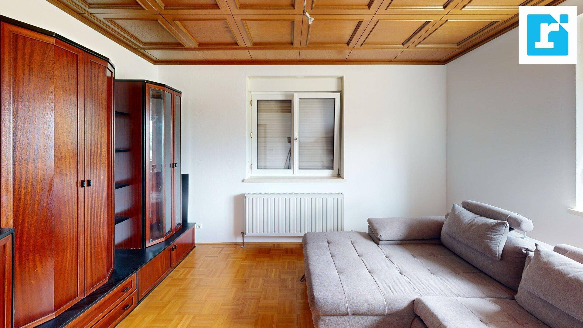 Helles Wohnzimmer mit Holzkassettendecke, Parkettboden und großem Schrank.