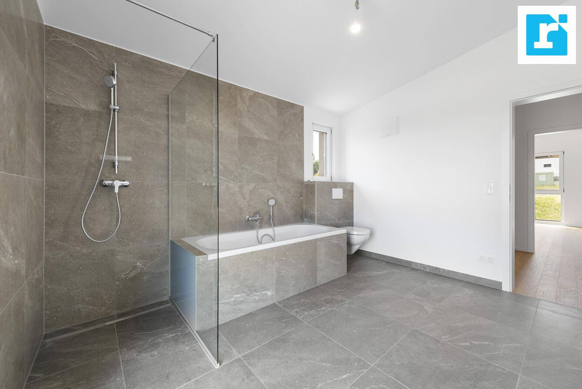Elegantes Badezimmer mit Badewanne, Dusche und wandhängendem WC, in neutralen Grautönen gehalten.