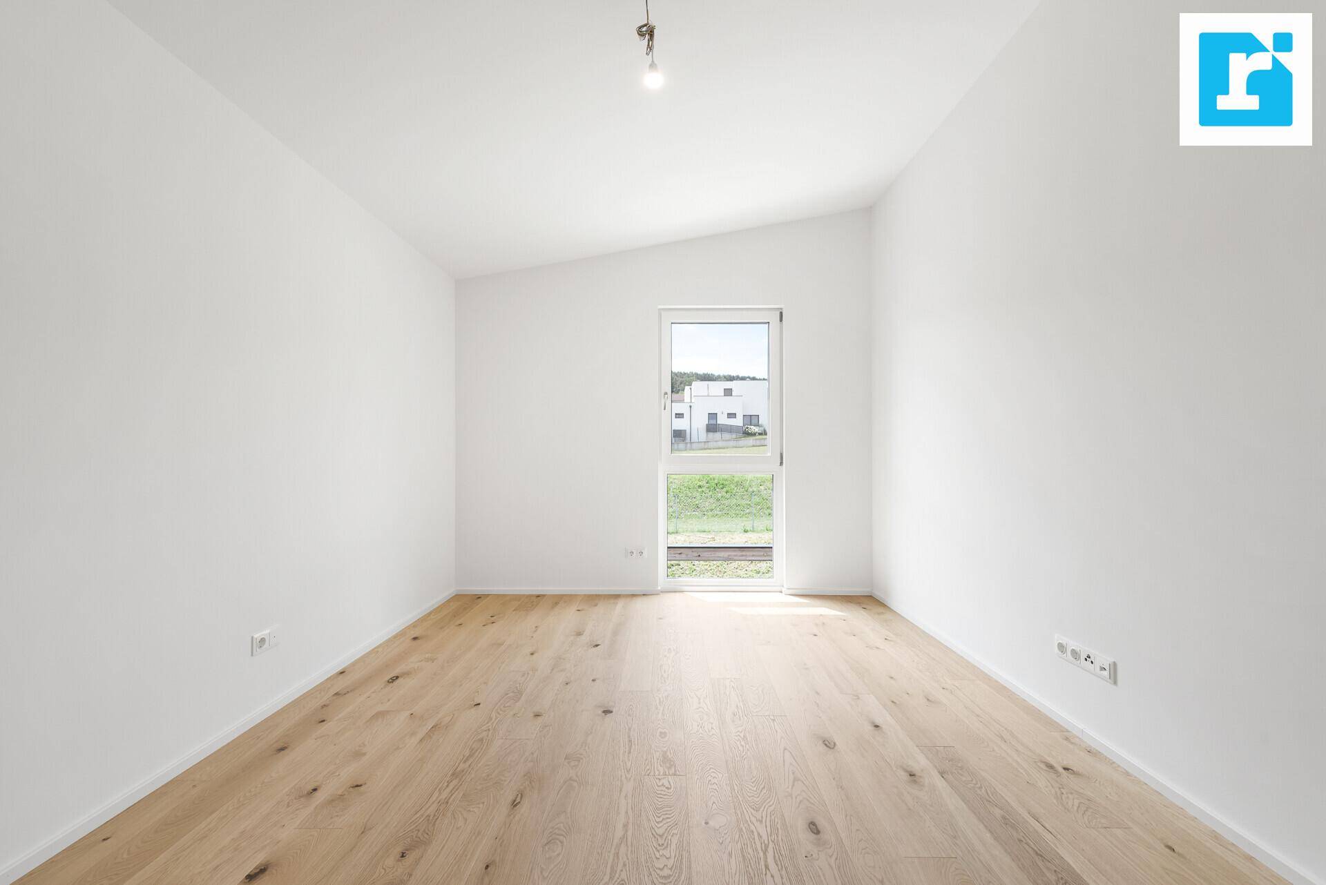 Lichtdurchflutetes Zimmer mit Holzboden und schräger Decke, bietet einen Ausblick ins Grüne.