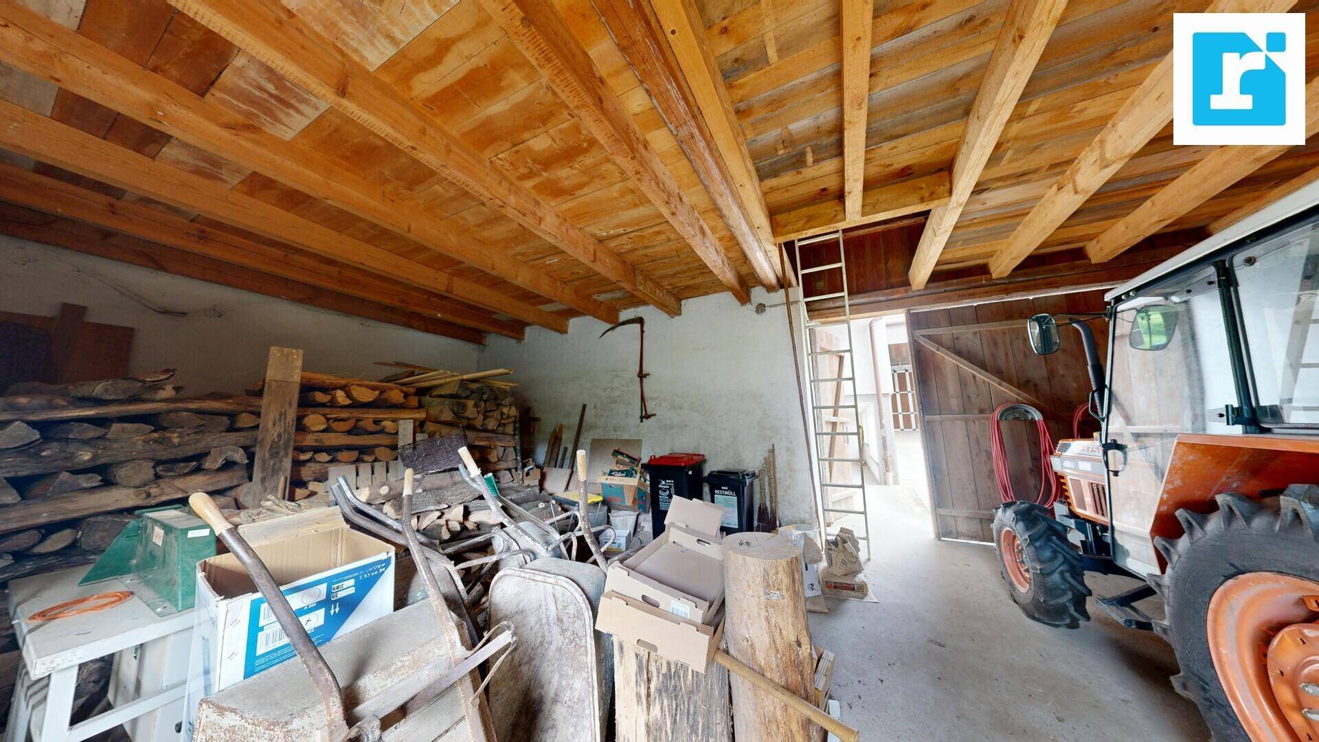Scheune oder Lagerraum mit Holzbalken, Brennholz und landwirtschaftlichen Geräten.