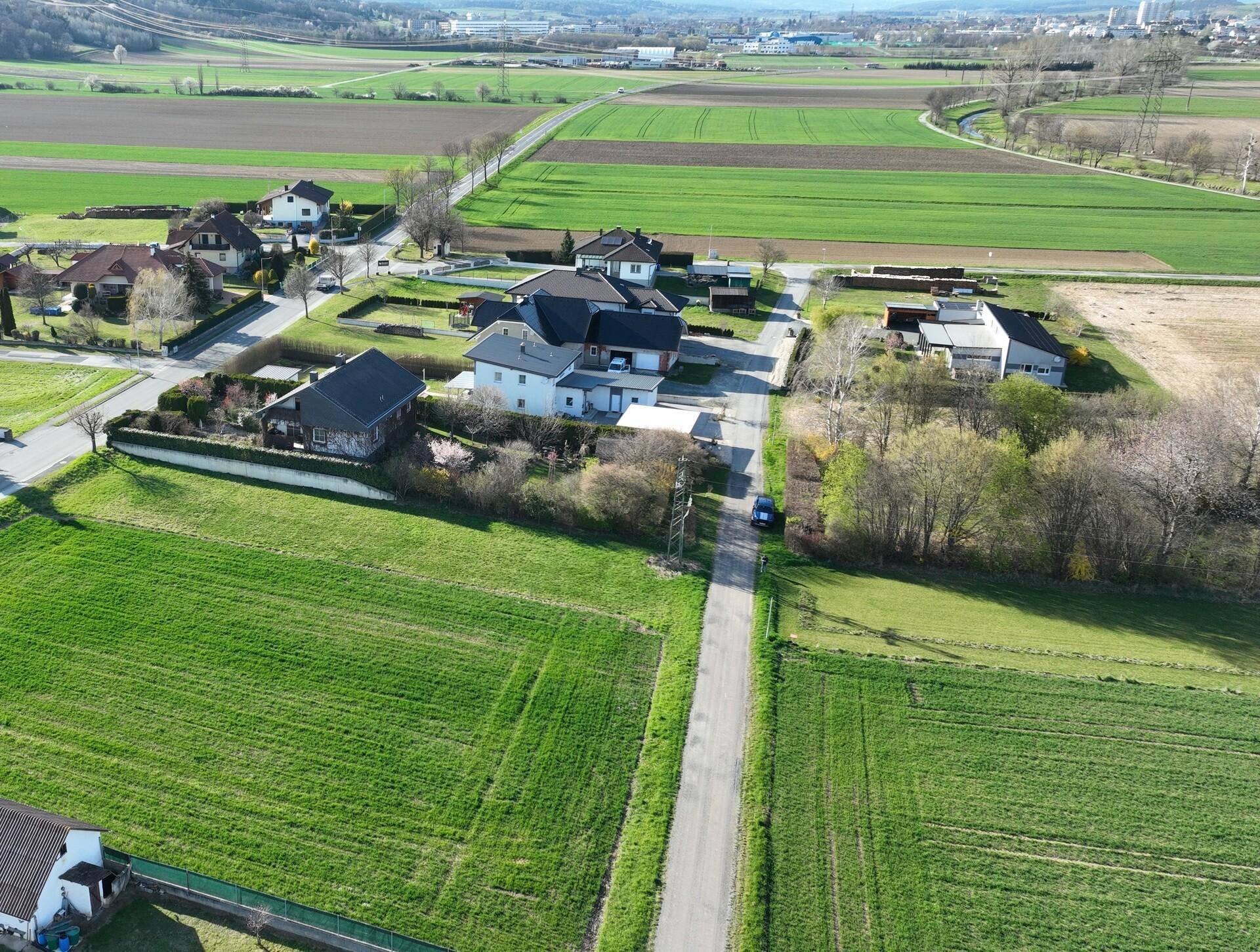 Weitläufige Luftansicht einer Wohnsiedlung umgeben von weiten grünen Feldern und ländlicher Landschaft.
