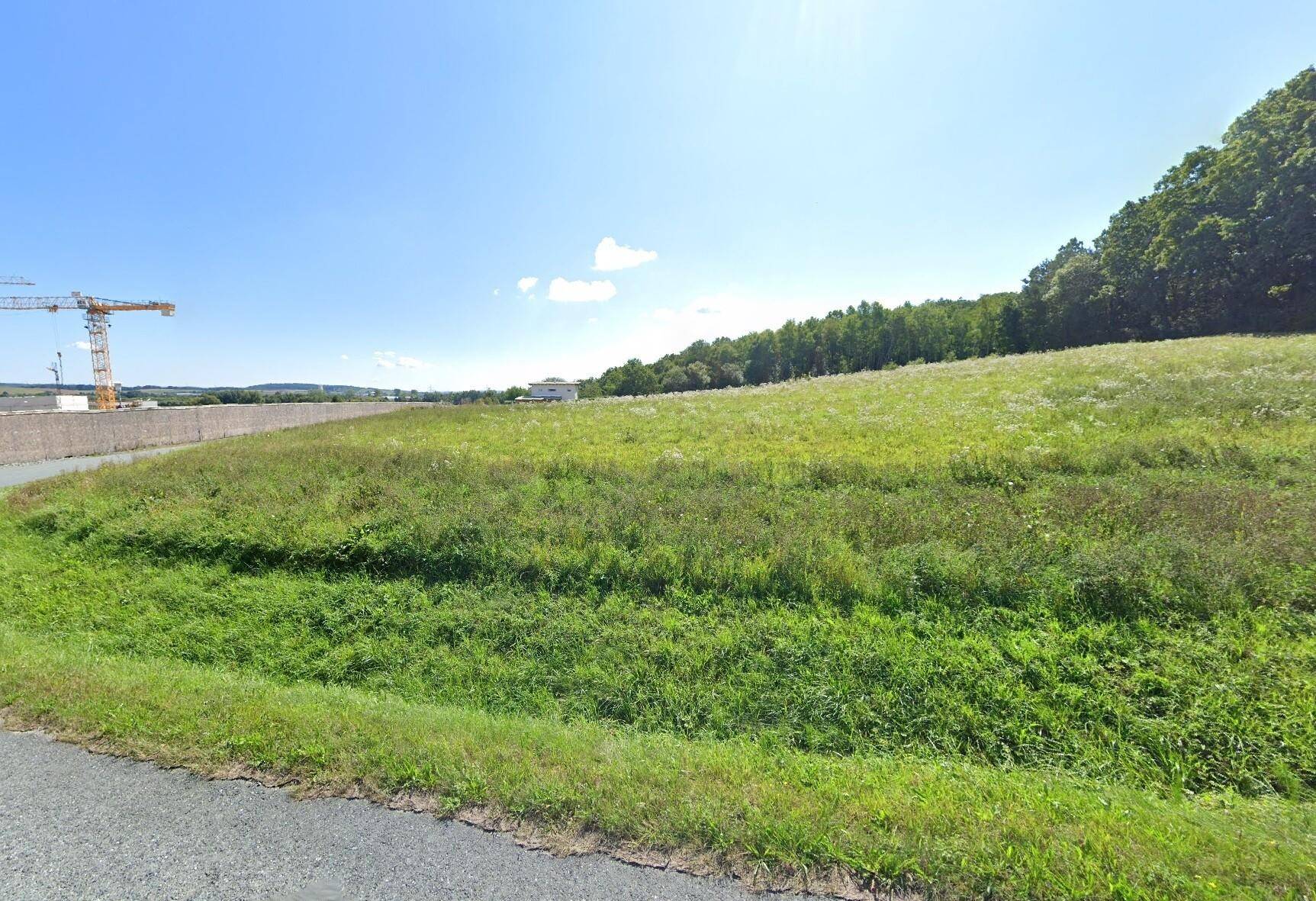 Grüne Wiese mit einem Baukran in der Ferne und bewaldeten Hügeln im Hintergrund.