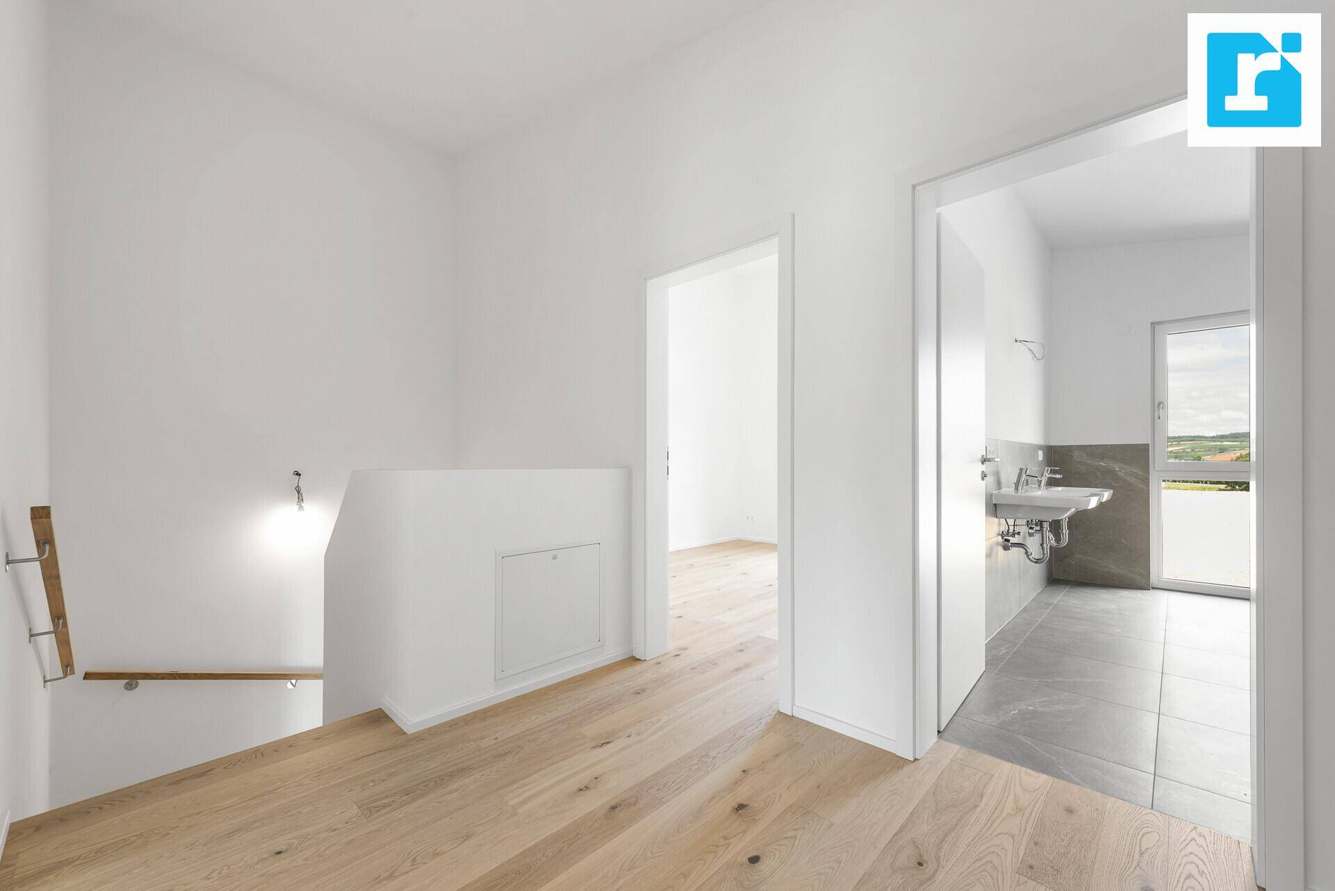 Geräumiger Flur mit Treppenabgang und Blick in ein modernes Badezimmer mit Fenster.