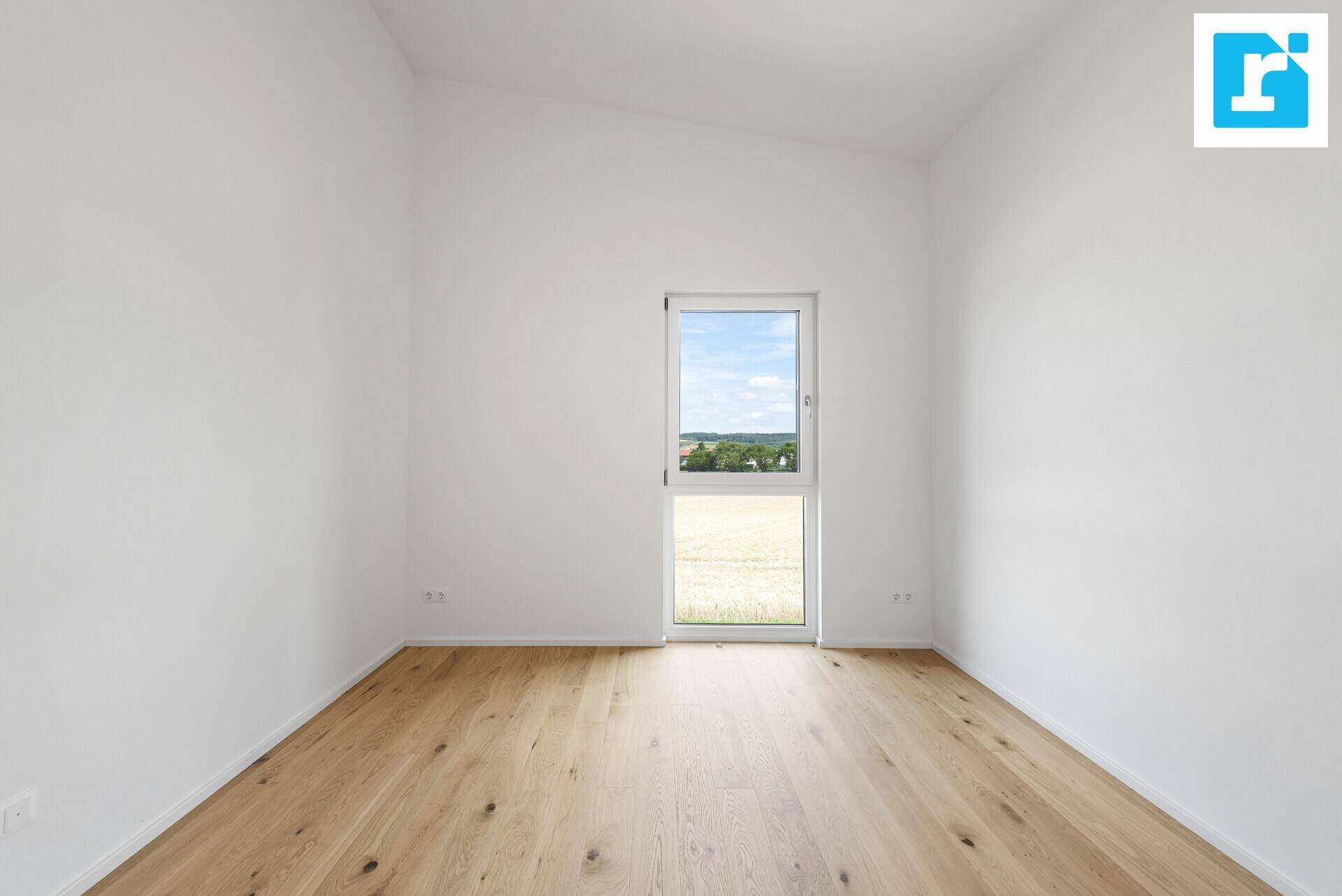 Helles Zimmer mit Holzboden und schräger Decke, bietet einen weiten Blick ins Grüne.