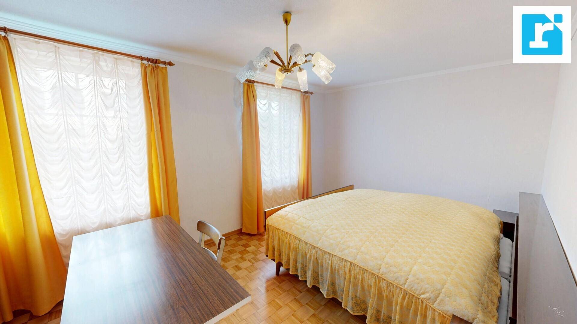 Schlafzimmer mit Doppelbett, Holzboden und gelben Vorhängen an den Fenstern.