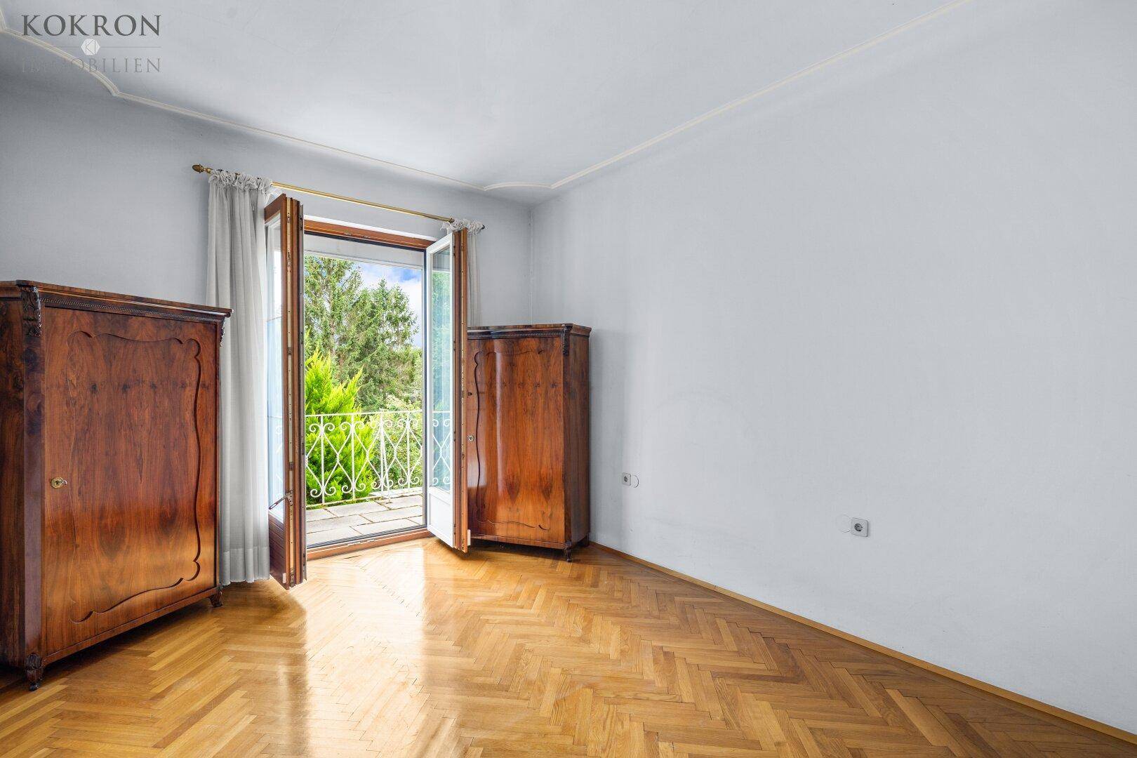 Schlafzimmer mit Fischgrätparkett, zwei Holzschränken und Zugang zu einem französischen Balkon.