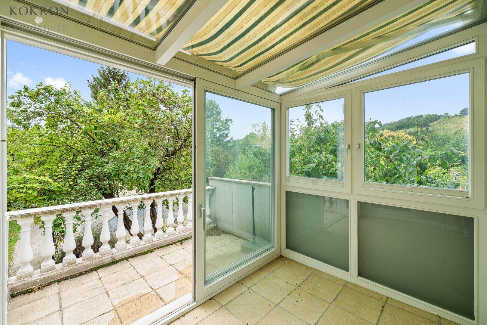 Heller Wintergarten mit großen Fenstern, Blick ins Grüne und Zugang zu einer kleinen Terrasse.