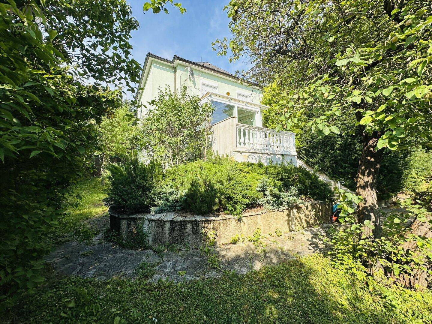 Charmantes Haus umgeben von üppigem Grün mit einem kleinen Balkon und Gartenbereich.