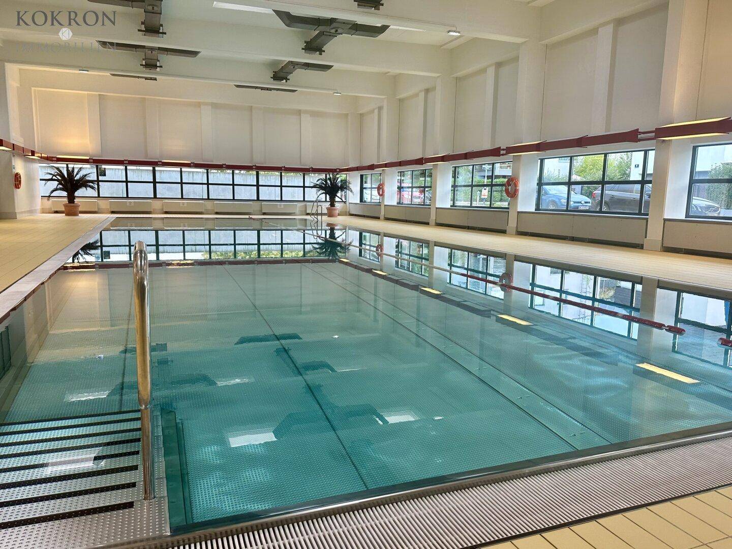 Großes Hallenbad mit natürlichem Lichteinfall und Blick ins Grüne, ideal für Sport und Entspannung.