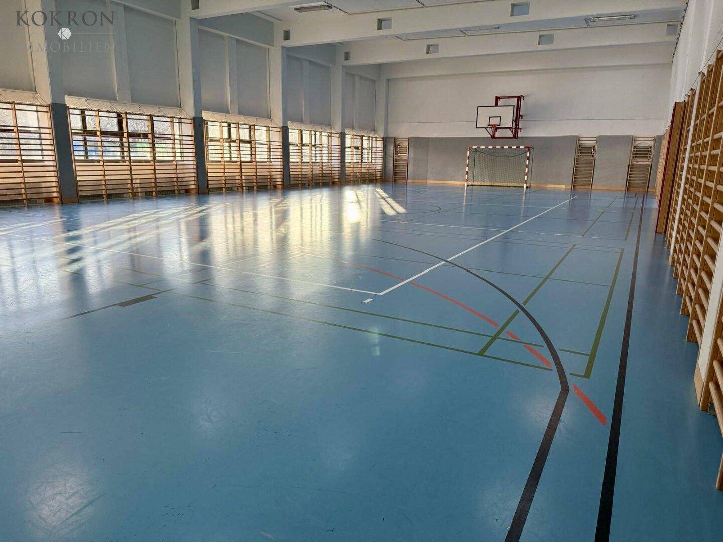 Große Sporthalle mit Linienmarkierungen und Sprossenwänden, ideal für verschiedene sportliche Aktivitäten.