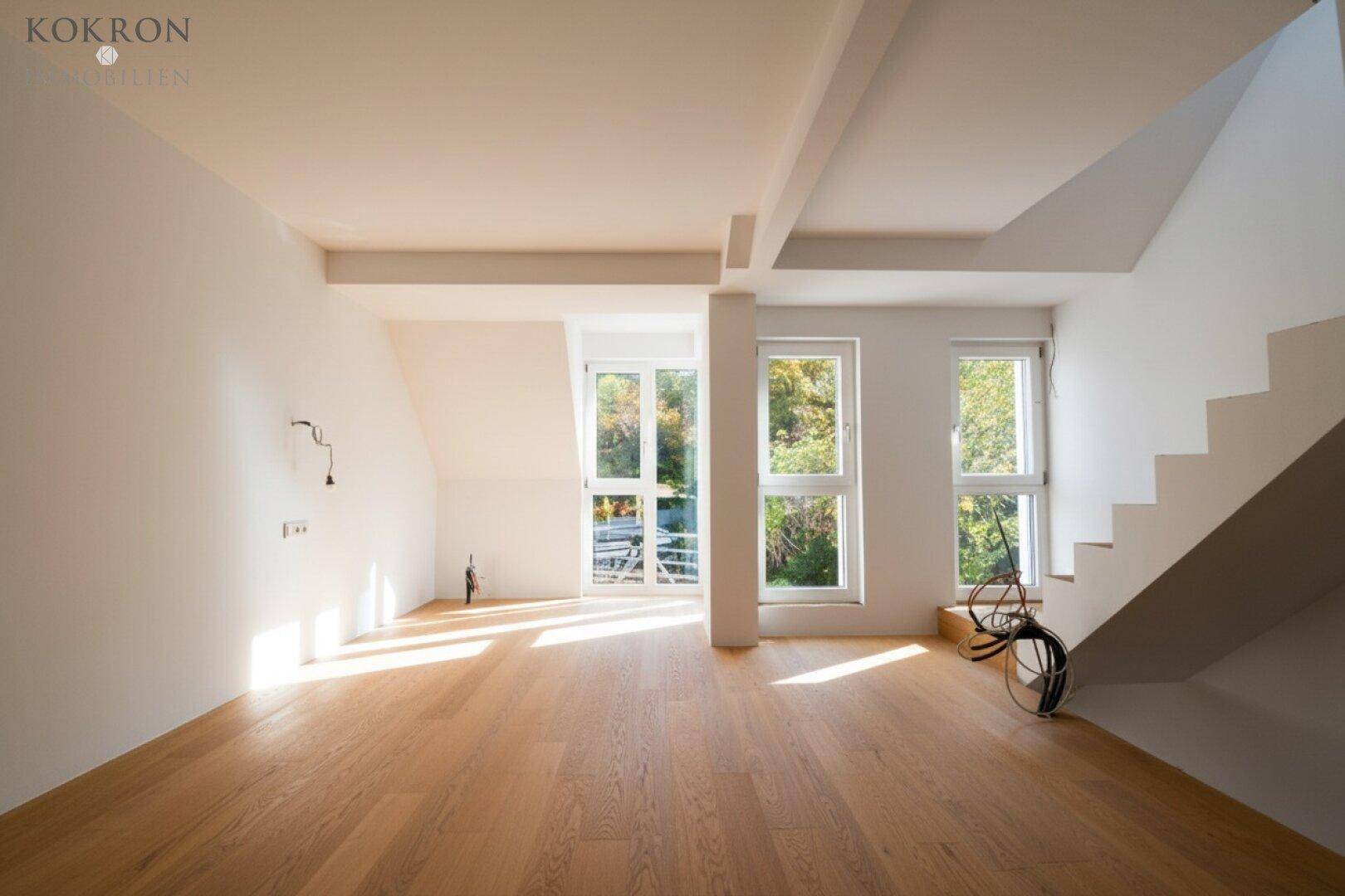 Lichtdurchfluteter Raum mit Holzboden, großen Fenstern und Blick ins Grüne.