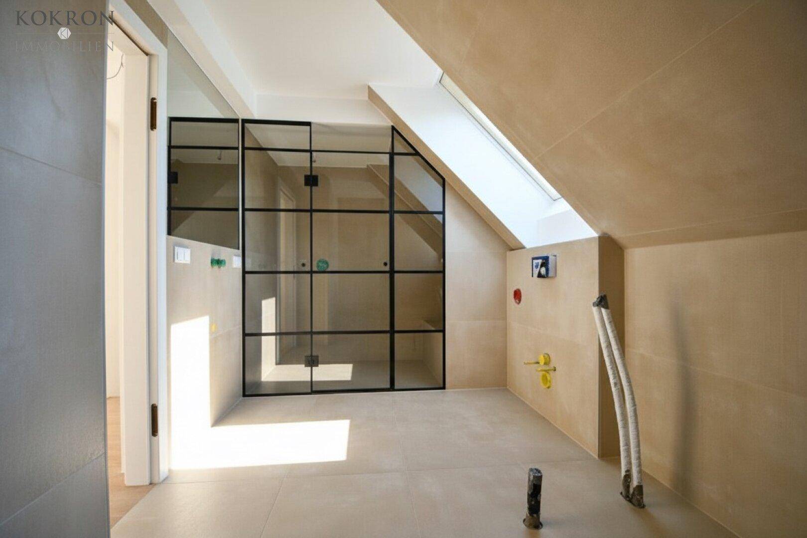 Badezimmer im Dachgeschoss mit Schrägdach, Oberlicht und moderner Glasabtrennung.