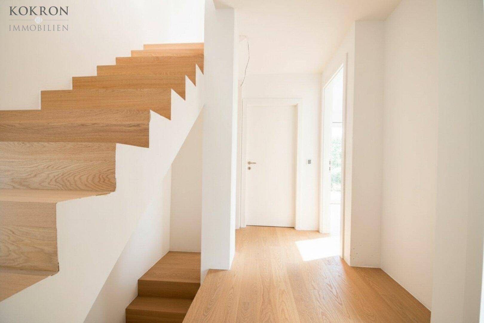 Heller Eingangsbereich mit offener Holztreppe und weiß gestrichenen Wänden.