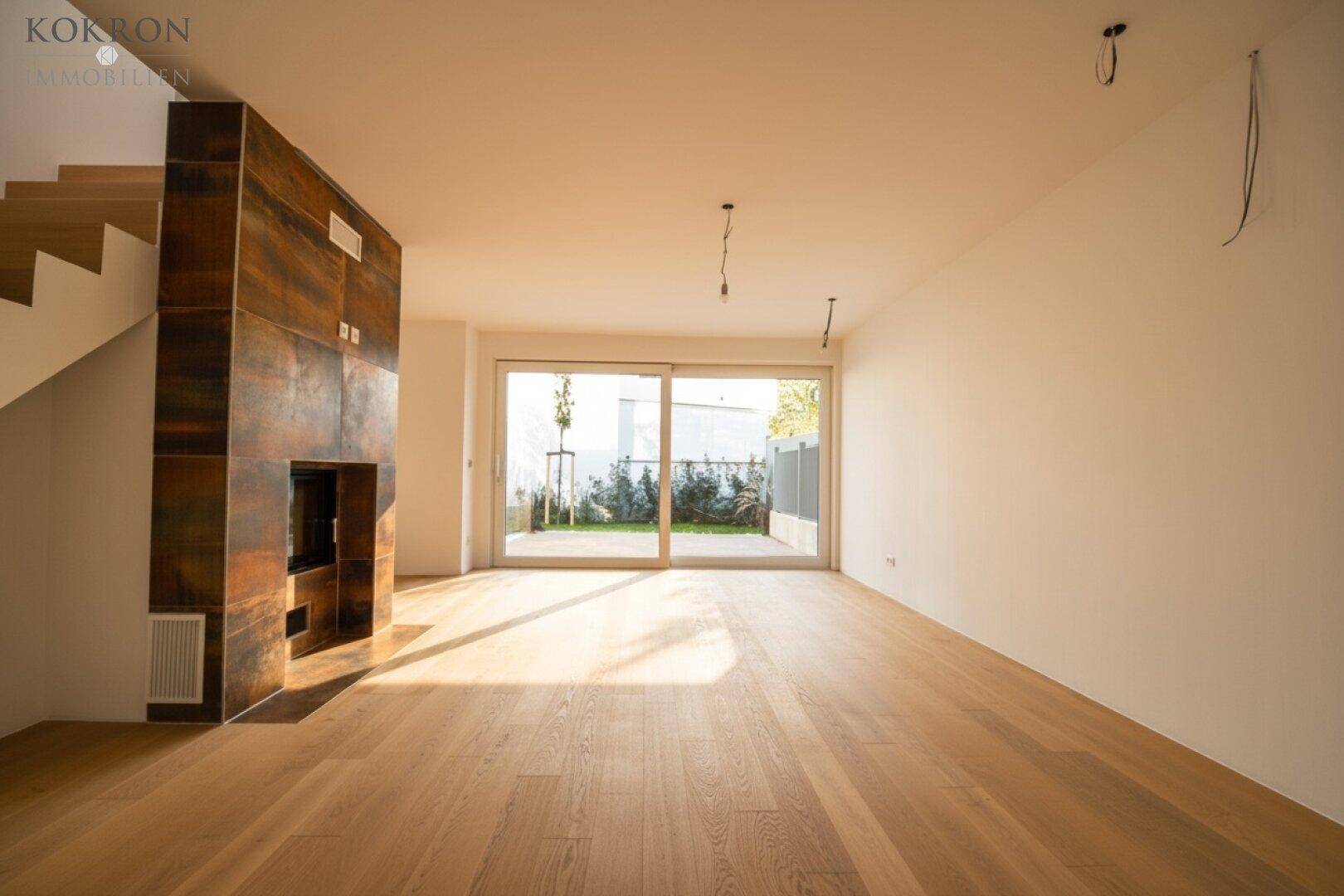 Geräumiges Wohnzimmer mit Holzboden, Kamin und großen Fenstern zum Außenbereich.