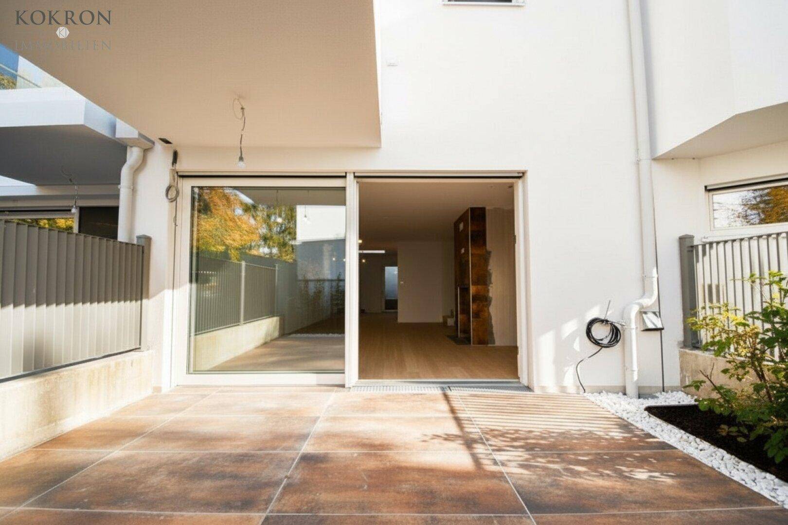 Sonniger Terrassenbereich mit großen Schiebetüren, die den Innenraum mit dem Garten verbinden.