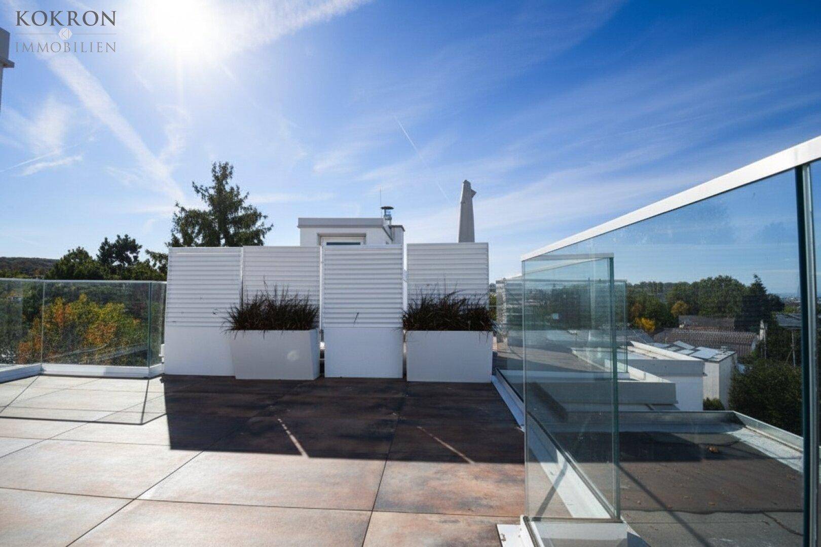 Sonnige Dachterrasse mit Glasgeländer und weitem Blick über die grüne Umgebung.