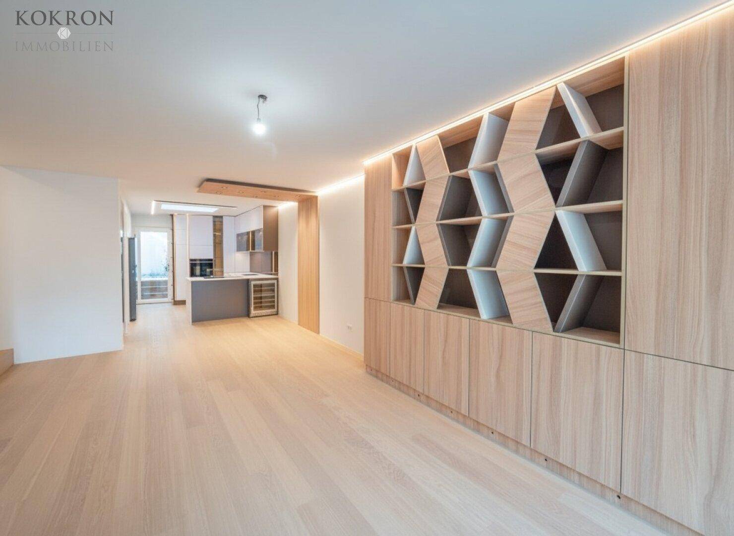 Geräumiger Wohnbereich mit Holzboden, dekorativem Regal und offenem Blick zur modernen Küche.