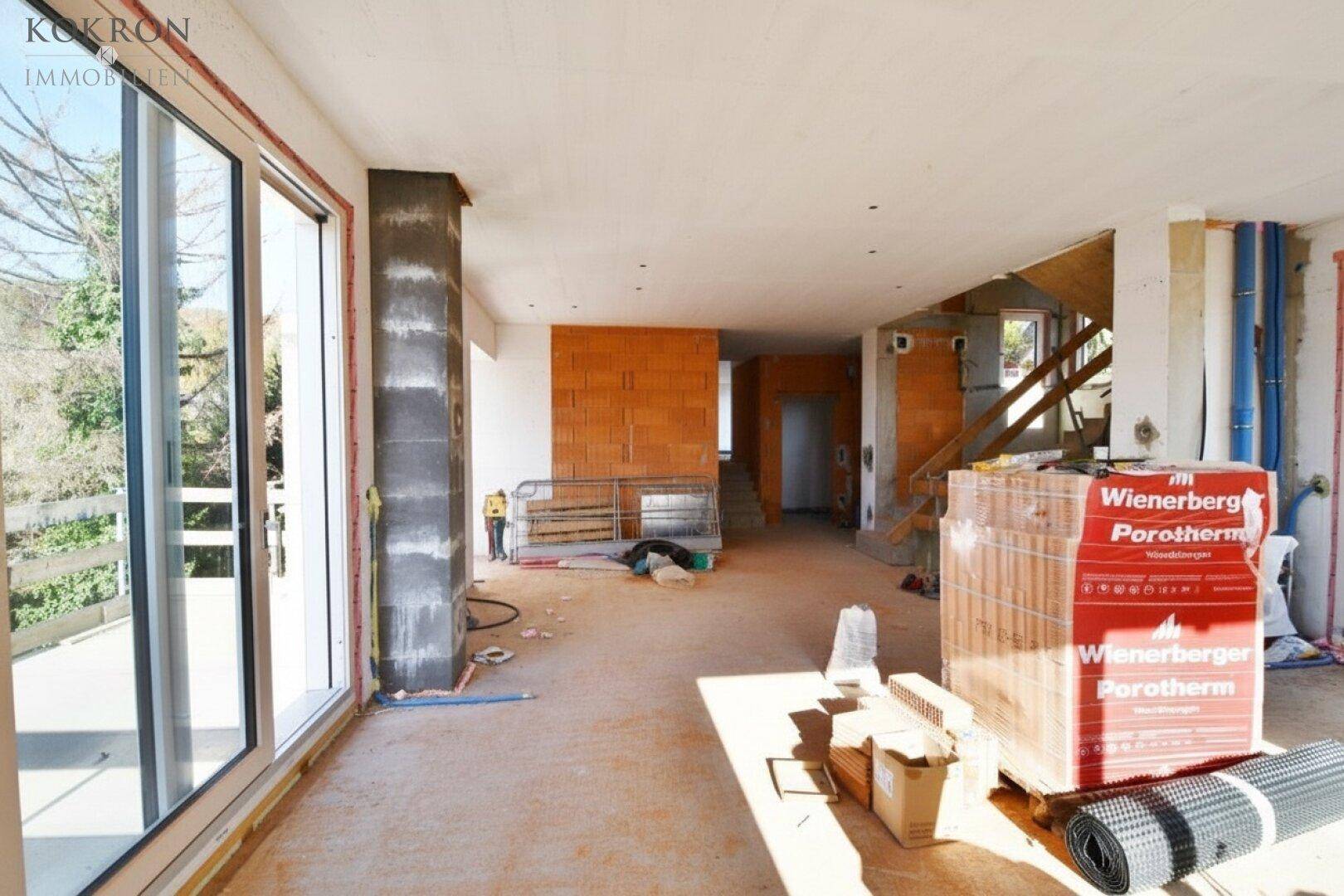 Innenansicht eines Rohbaus mit großen Fensteröffnungen und sichtbaren Ziegelwänden.
