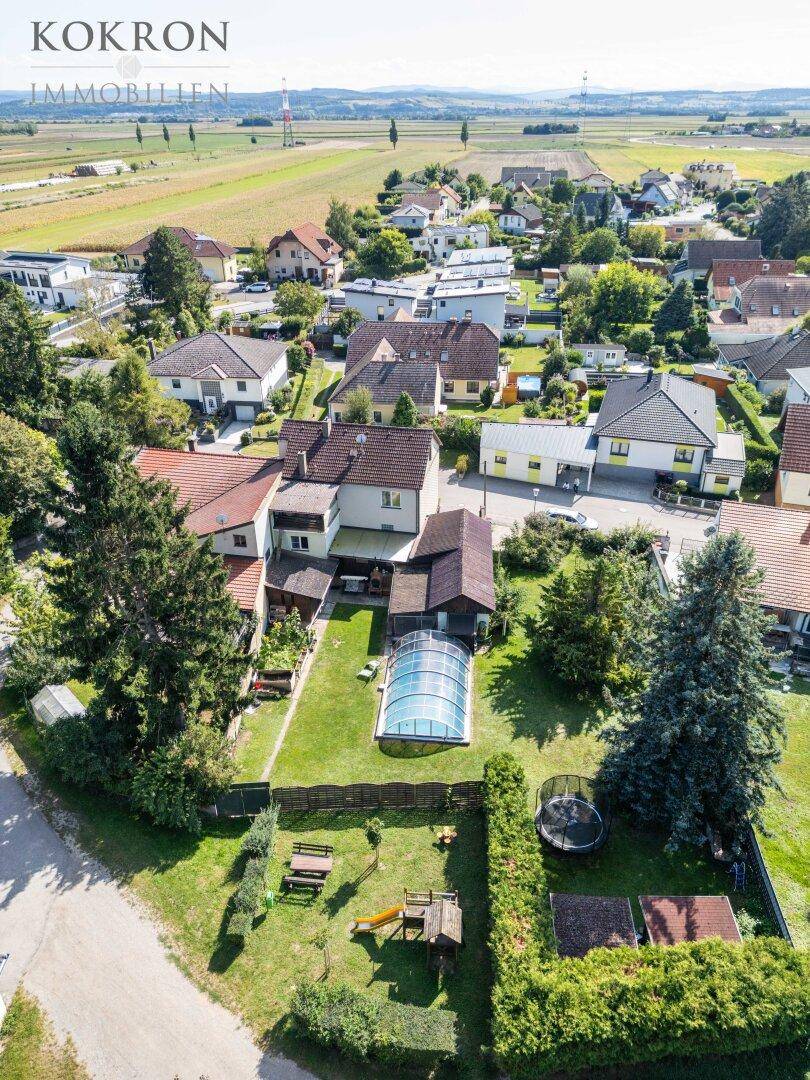 Luftaufnahme eines Wohnhauses mit Garten, Pool, Trampolin und Spielplatz in ländlicher Umgebung.