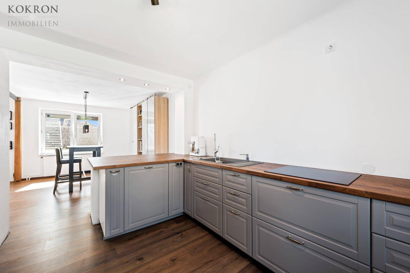 Moderne Küche mit grauen Schränken, Holzarbeitsplatte und Blick auf den Essbereich.