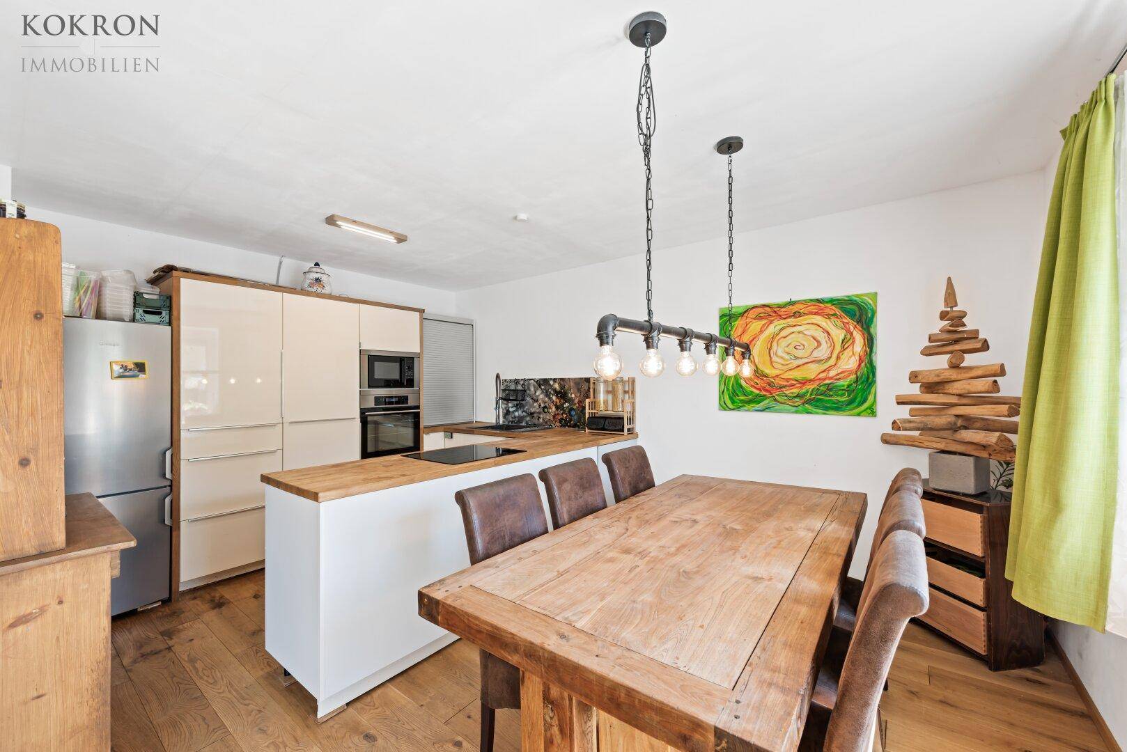 Helle Küche mit Holzboden und Essbereich, ausgestattet mit modernen Geräten und Kühlschrank.