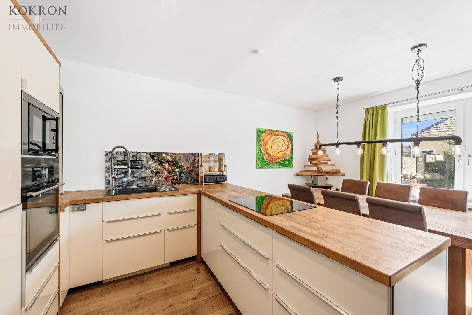 Moderne Küche mit hellen Fronten, Holzarbeitsplatten und integrierten Geräten, offen zum Essbereich.