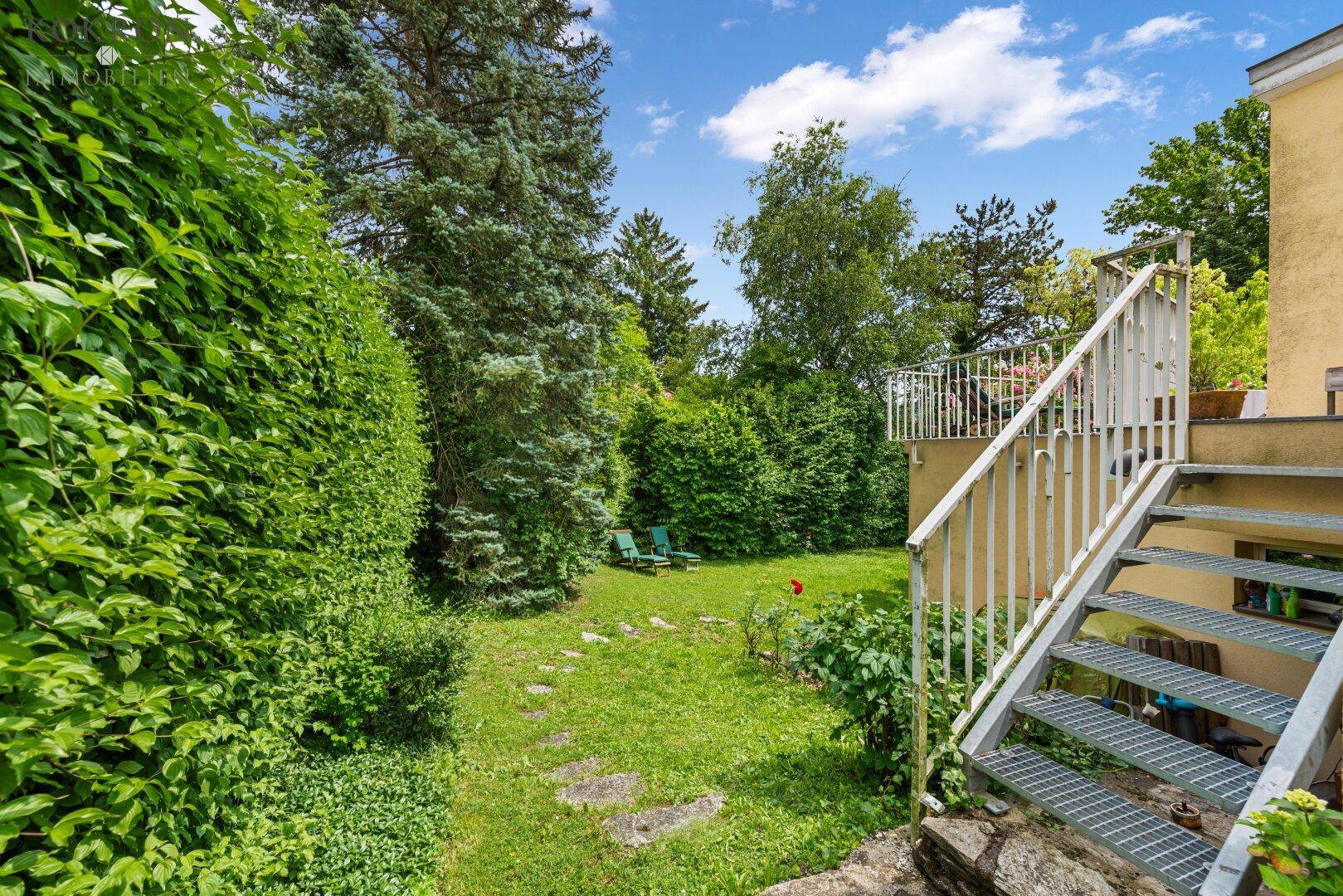 Gepflegter Garten mit Rasenfläche und einer Metalltreppe, die zur oberen Terrasse führt.