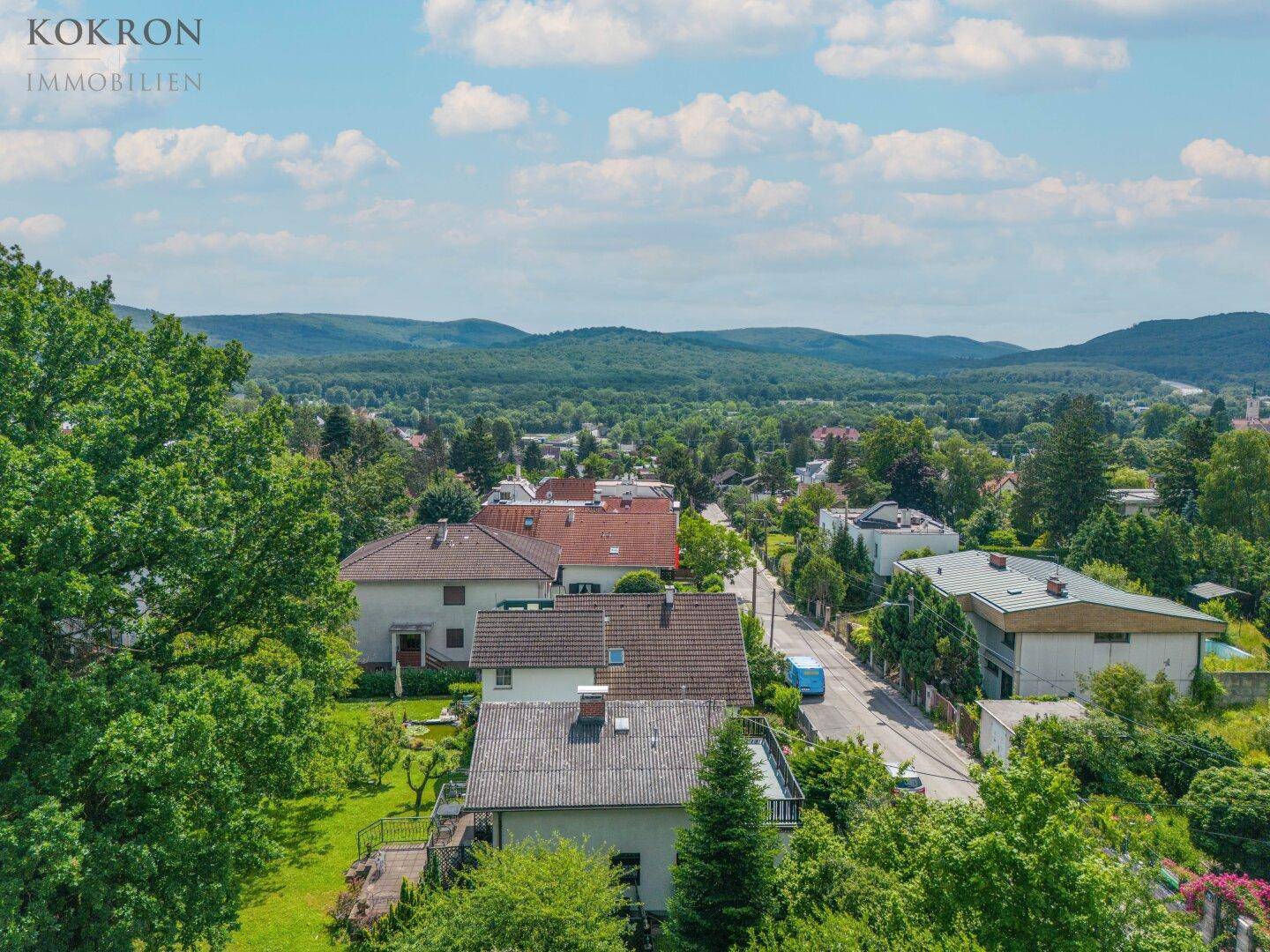 Weitläufige Luftaufnahme der Wohngegend mit grünen Hügeln und Wäldern im Hintergrund.