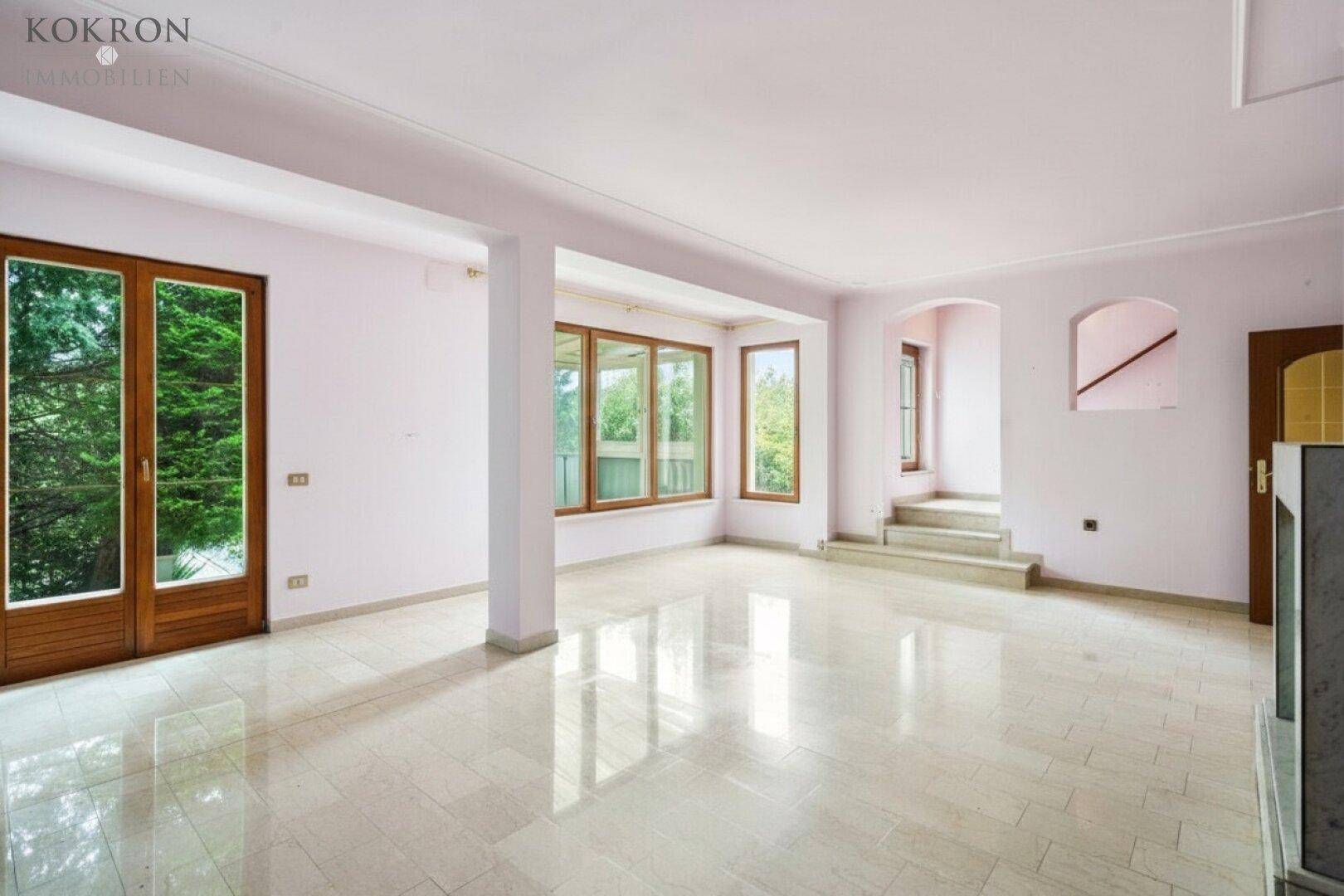 Geräumiges, leeres Wohnzimmer mit hellrosa Wänden, großen Fenstern und glänzendem Fliesenboden.