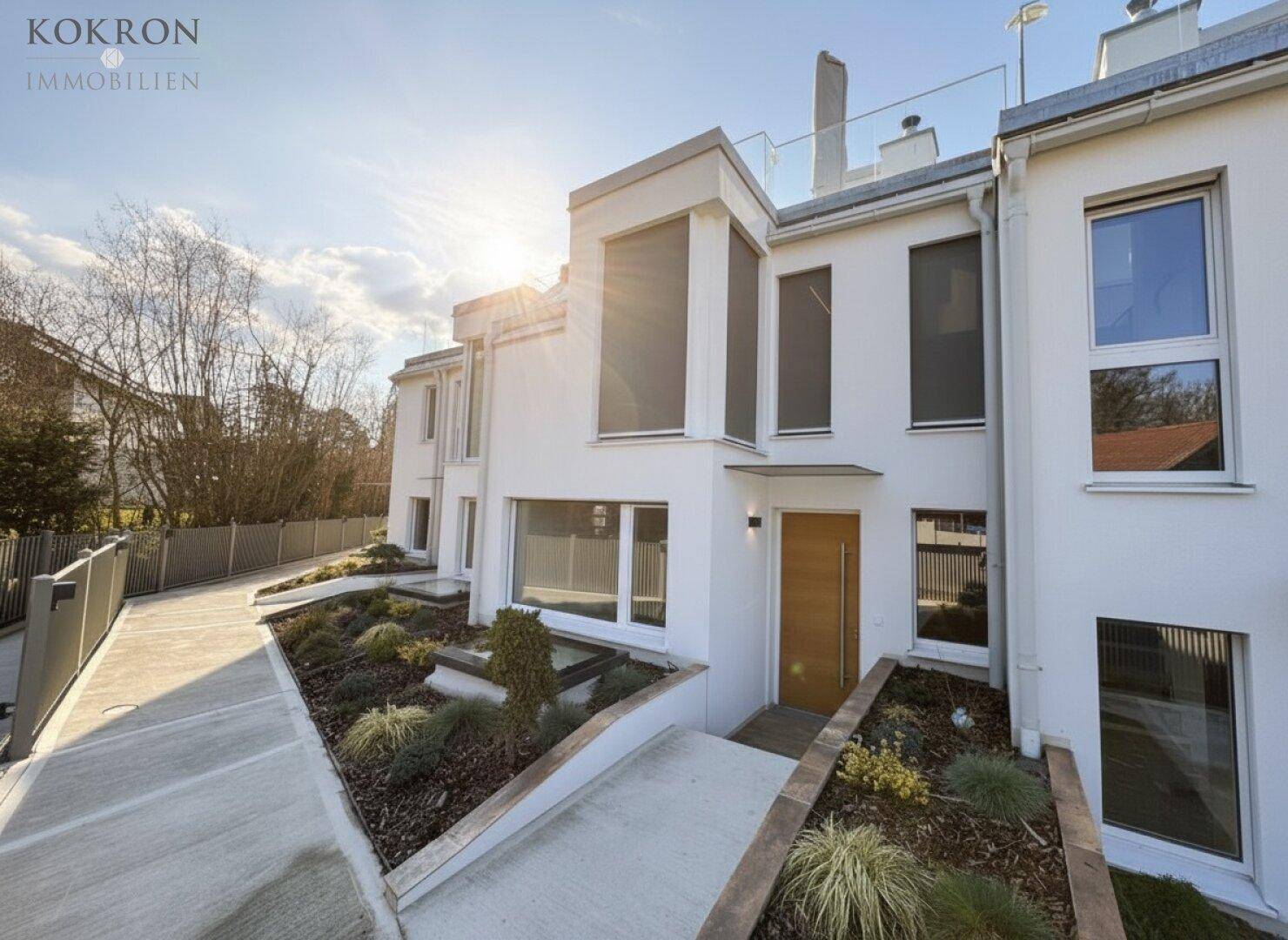 Zeitgenössisches Gebäude mit weißer Fassade, großen Fenstern und gepflegter Außenanlage.