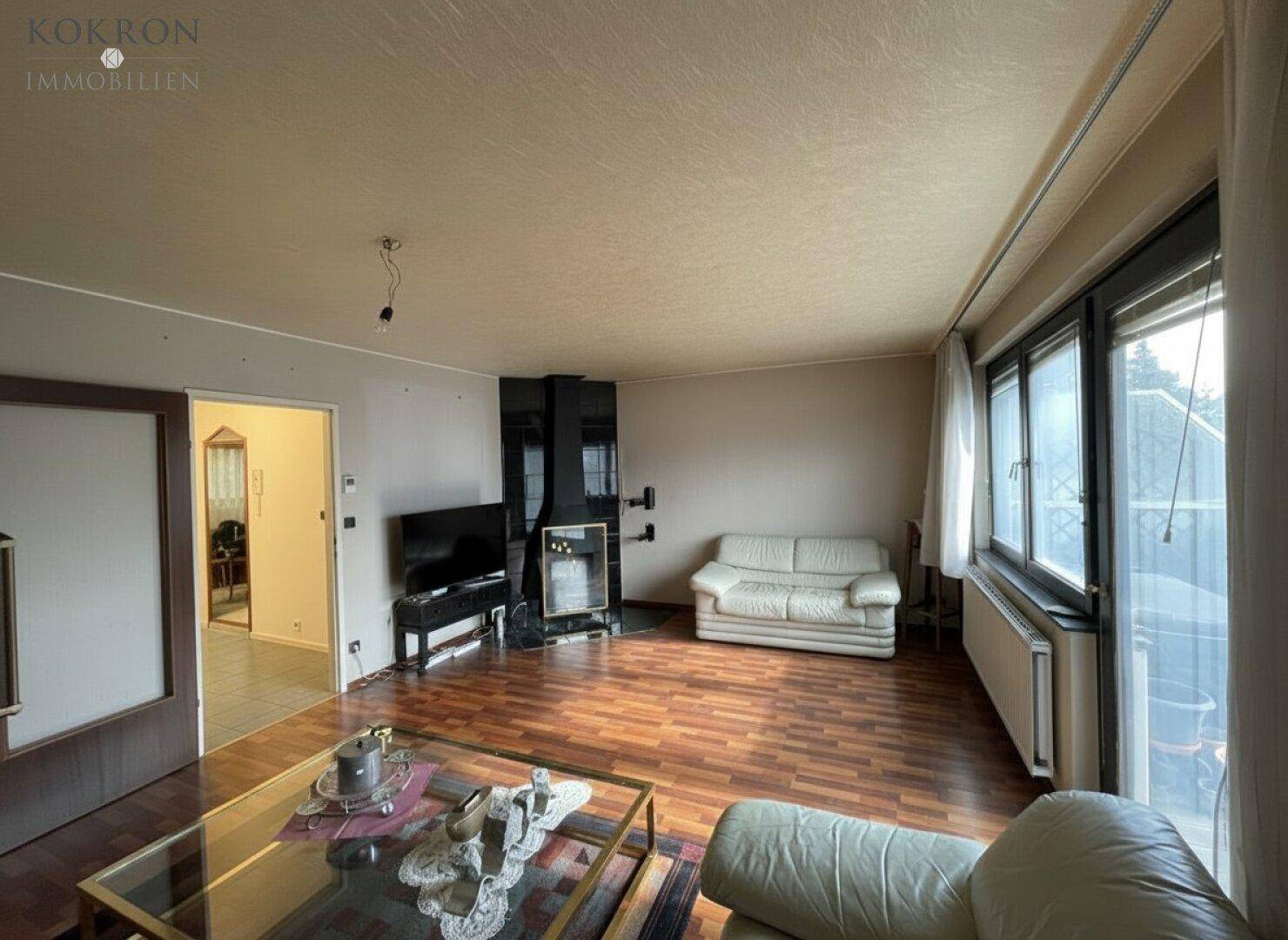 Geräumiges Wohnzimmer mit Parkettboden, Kamin und großen Fenstern.