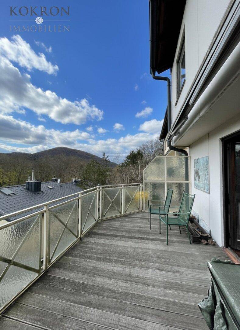 Sonniger Balkon mit Holzboden, Glasgeländer und Panoramablick auf die Berge.
