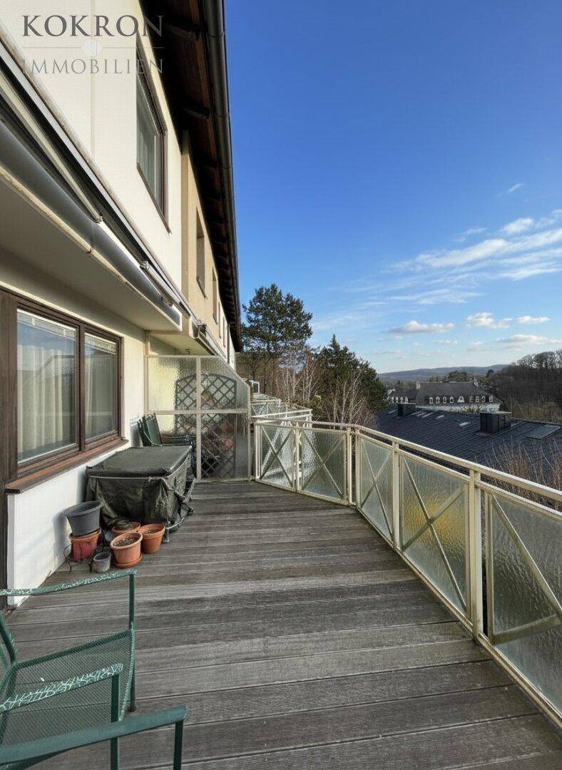 Langer Balkon mit Holzboden, Glasgeländer und weitem Blick ins Grüne.