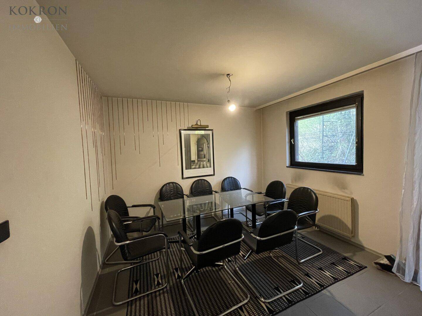 Esszimmer mit großem Glastisch, mehreren Stühlen und Fensterblick ins Grüne.