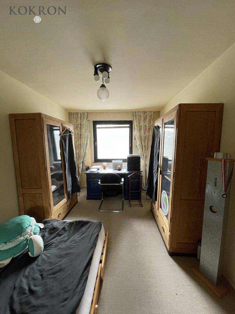 Schlafzimmer mit Bett, Holzschränken und Fenster mit Vorhängen.