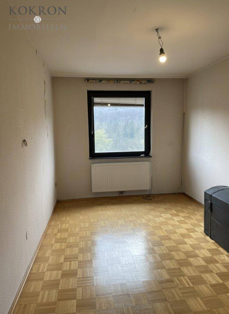 Helles Schlafzimmer mit Parkettboden, großem Fenster und Heizkörper.