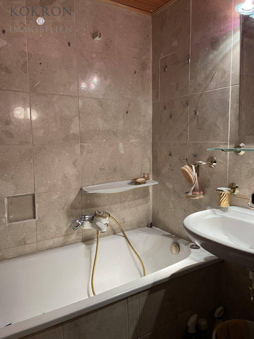 Gefliestes Badezimmer mit Badewanne, Waschbecken und Holzdecke.