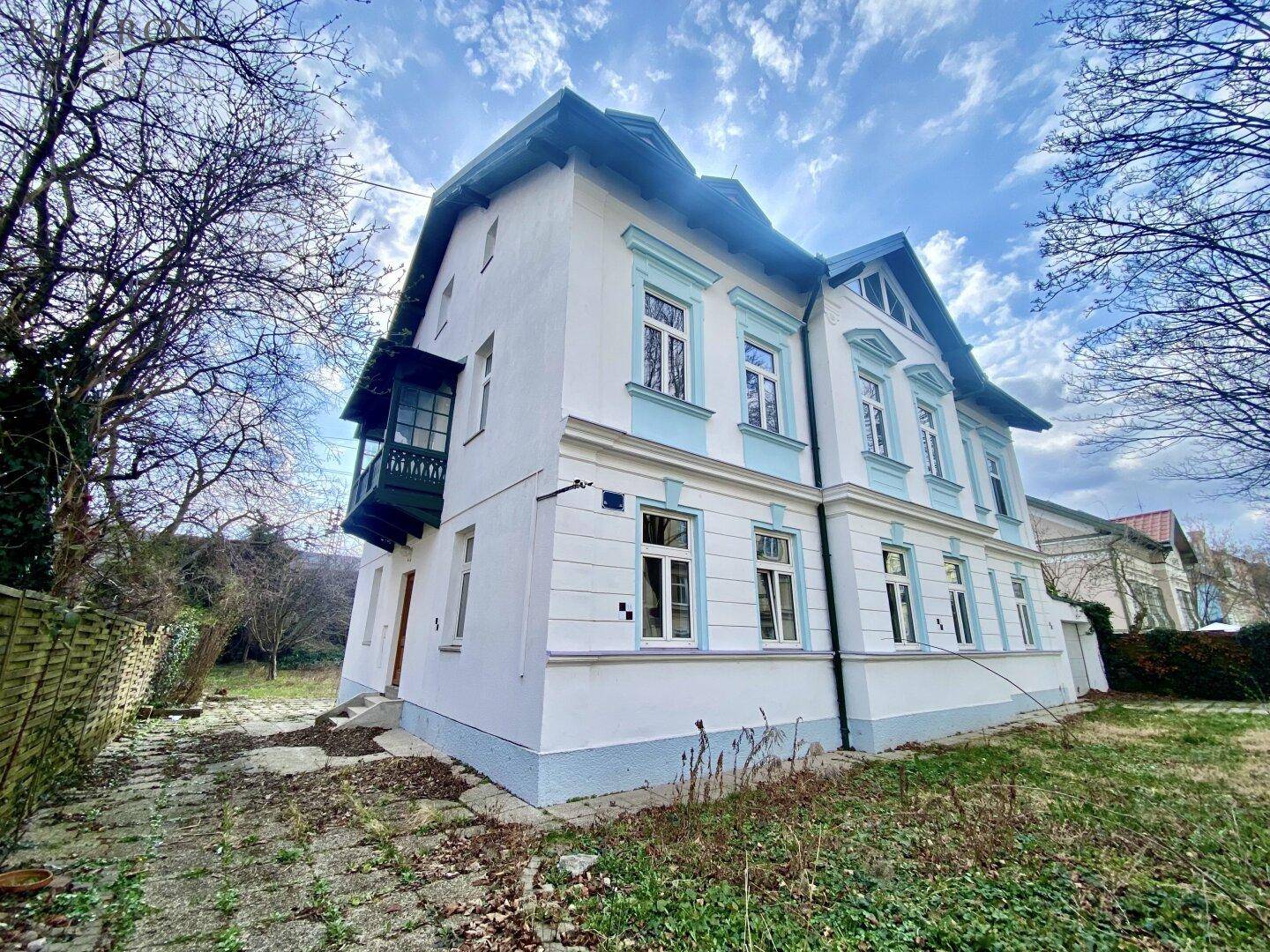 Seitenansicht des historischen Gebäudes mit Erker und Gartenbereich unter bewölktem Himmel.