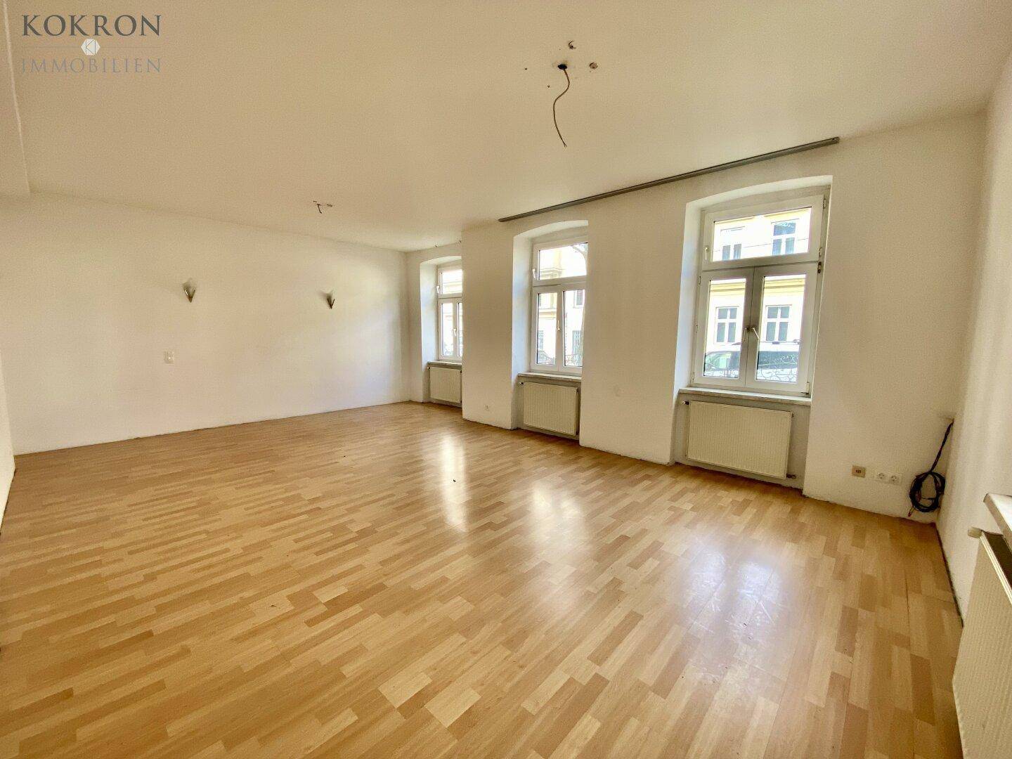 Lichtdurchfluteter Raum mit hellem Parkettboden und mehreren Fenstern.
