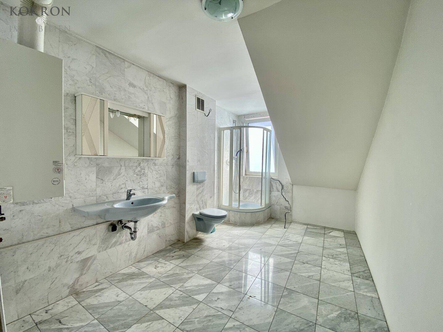 Badezimmer mit Marmorfliesen, Dusche und Dachschräge unter einem Dachfenster.