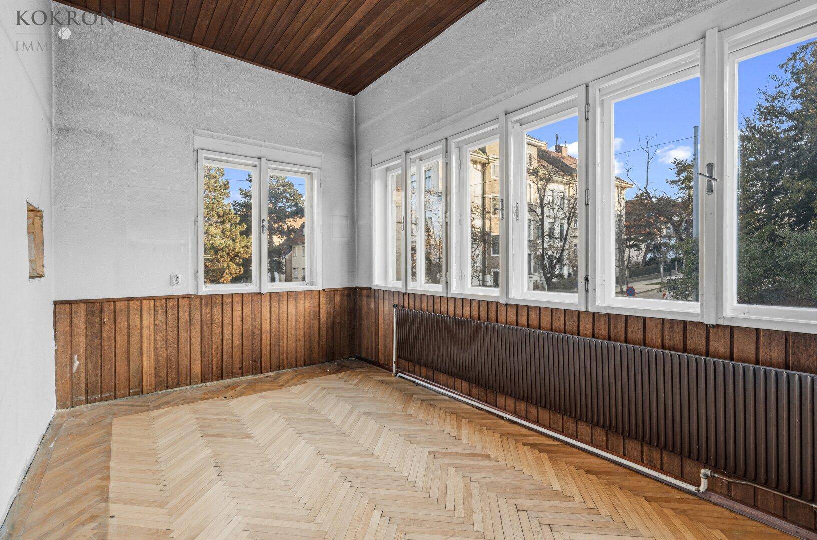 Gemütlicher Raum mit Holzvertäfelung, Holzbalkendecke und Fischgrätparkett, umgeben von Fenstern.