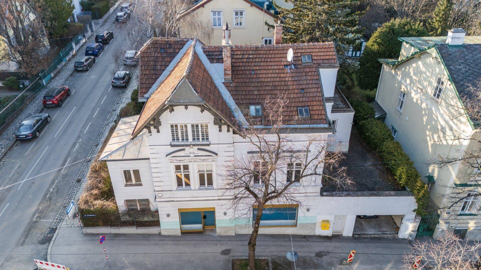Luftaufnahme des historischen Gebäudes mit Ziegeldach, Garage und der umliegenden Straßenstruktur.