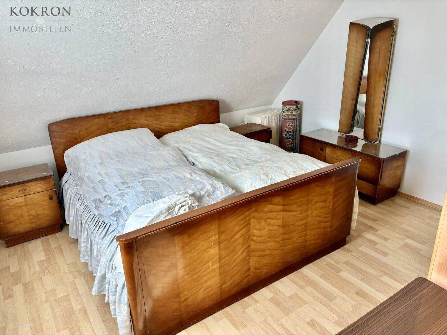 Schlafzimmer mit Holzbett, passenden Nachttischen und Kommode unter einer Dachschräge.